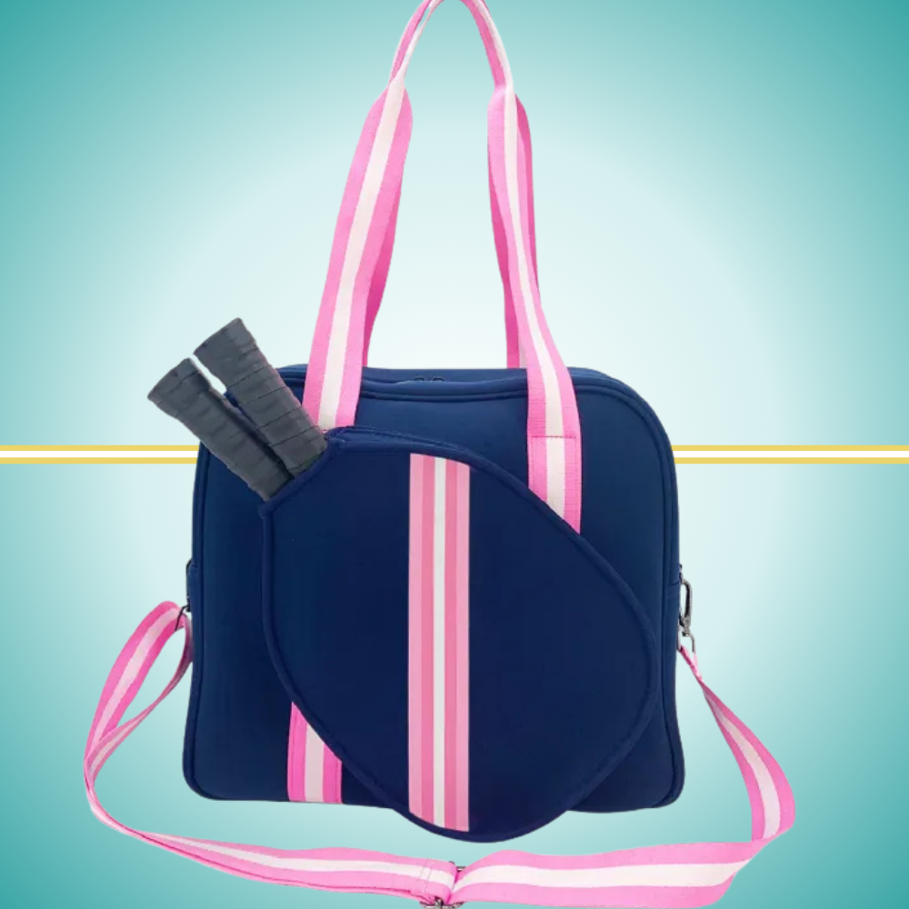 Navy women's pickleball tote bag with pink stripes, top handles, adjustable crossbody strap, and attached front paddle cover.