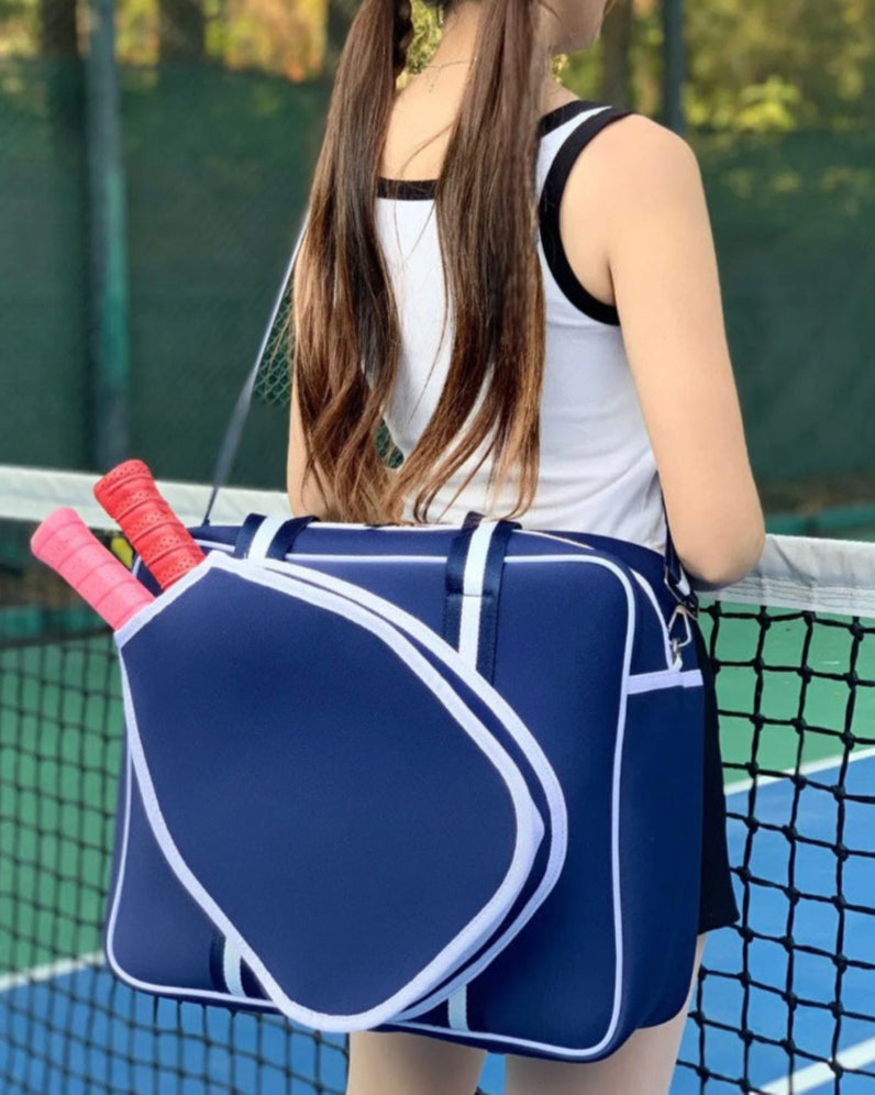 Navy women's pickleball tote bag with 
 white stripes, top handles, adjustable crossbody strap, and attached front paddle cover, this is a lifestyle picture with a model wearing it
