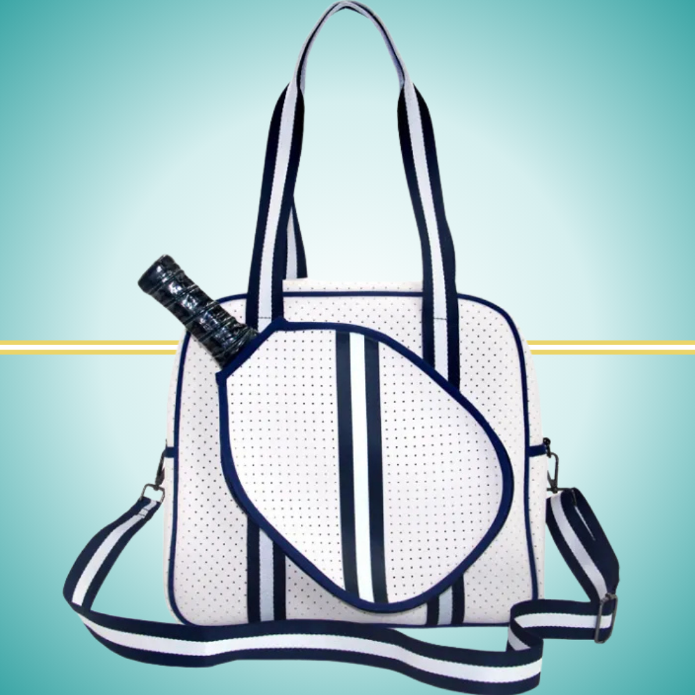 White women's pickleball tote bag with navy stripes, top handles, adjustable crossbody strap, and attached front paddle cover.