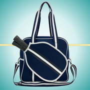 Navy women's pickleball tote bag with 
 white stripes, top handles, adjustable crossbody strap, and attached front paddle cover.