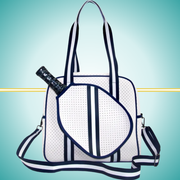 White women's pickleball tote bag with navy stripes, top handles, adjustable crossbody strap, and attached front paddle cover.